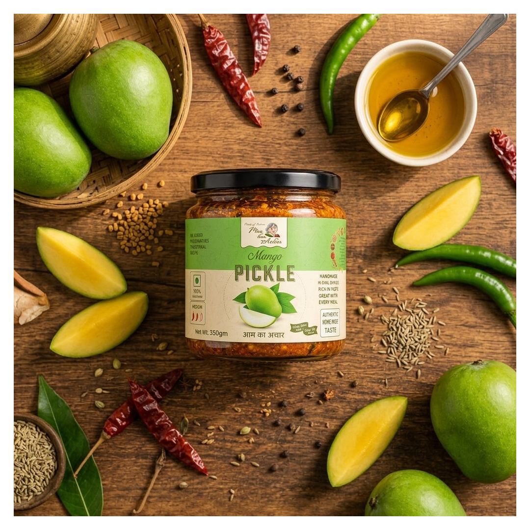 A jar of Mango Pickle from Pure Pickles is displayed on a rustic wooden table surrounded by fresh ingredients including whole and sliced green mangoes, dried red chilies, green chilies, cumin seeds, and a small bowl of golden oil with a spoon.