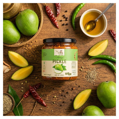 A jar of Mango Pickle from Pure Pickles is displayed on a rustic wooden table surrounded by fresh ingredients including whole and sliced green mangoes, dried red chilies, green chilies, cumin seeds, and a small bowl of golden oil with a spoon.
