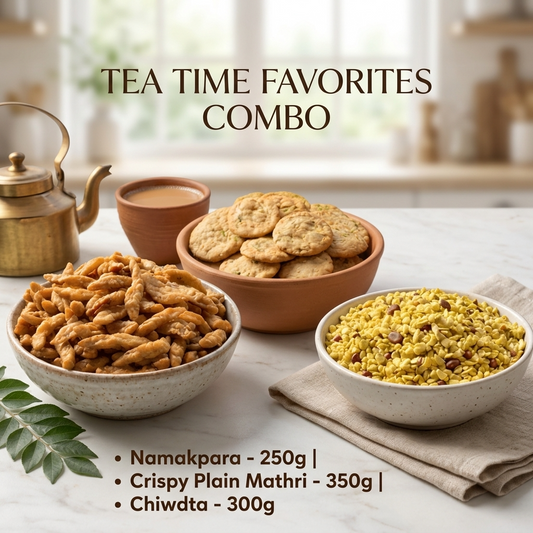 A styled tea-time snack assortment on a light marble surface with a blurred kitchen background. Bowls and cups contain samosas, cookies, and a yellow spice mix, with a brass teapot and a cup of tea.