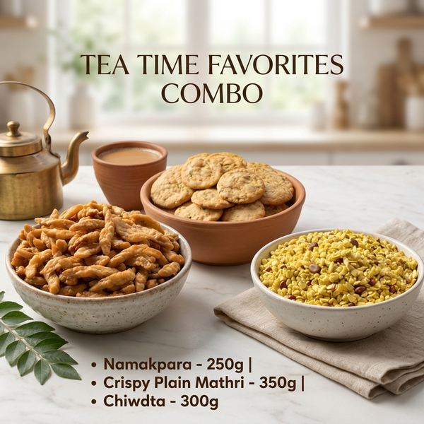 A styled tea-time snack assortment on a light marble surface with a blurred kitchen background. Bowls and cups contain samosas, cookies, and a yellow spice mix, with a brass teapot and a cup of tea.